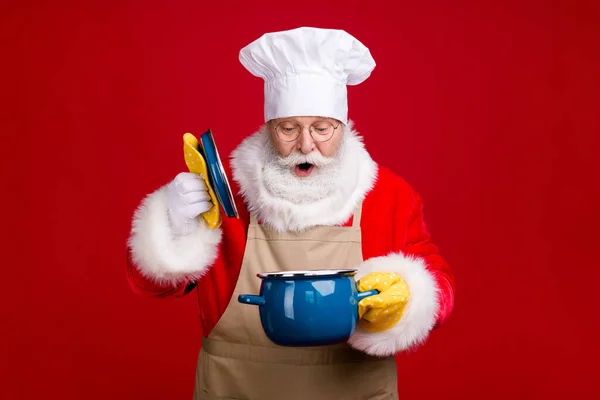 Zdjęcie zdumiony Santa Claus otwarte pokrycie garnek rondel x-mas przegotowana kolacja nosić cahef cap czerwony fartuch odizolowany jasny połysk kolor tło — Zdjęcie stockowe