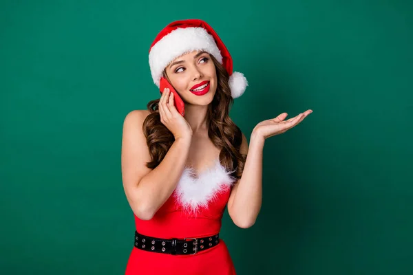 Fotografie atraktivní Santa asistent dáma držet telefon příjem objednávky dárky doručení služby říci zákazník ceník nosit červený sníh dívka šaty x-mas čepice izolované zelené barvy pozadí — Stock fotografie