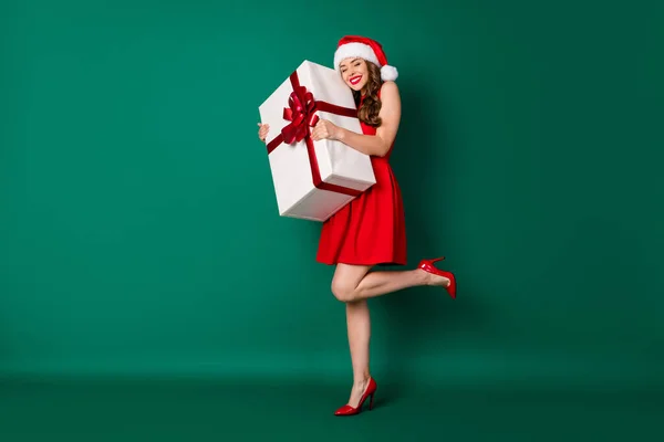 Omg, não acredito. Foto em tamanho completo bonito doce menina em santa claus headwear abraço desfrutar de grande x-mas milagre magia giftbox desgaste saia pernas salto alto isolado cor verde fundo — Fotografia de Stock