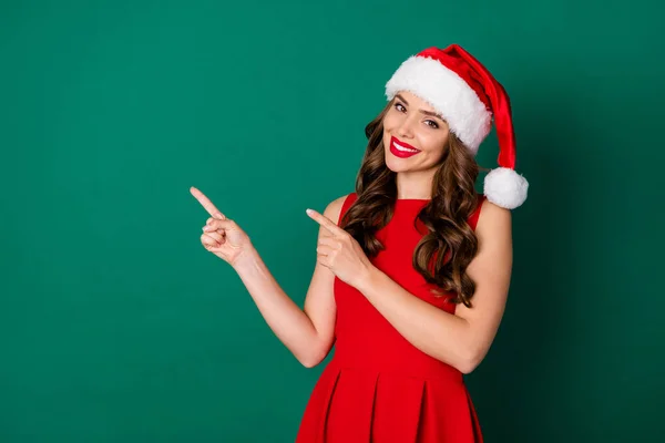 Fotografie okouzlující krásná hezká hezká dívka v Santa Claus headwear bod ukazováček copyspace indikovat x-mas veselý cesmína reklama oblečení sukně izolované přes zelenou barvu pozadí — Stock fotografie