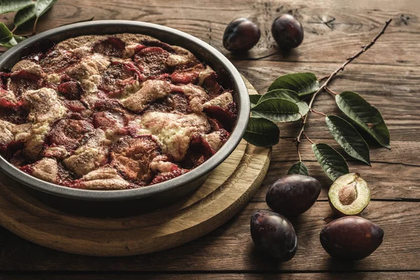 Plum cake caramelized and plums on wood backgraund. Round tart decorated by fruits and leaves