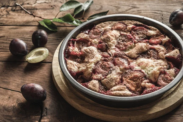 Plum cake caramelized and plums on wood backgraund. Round tart decorated by fruits and leaves