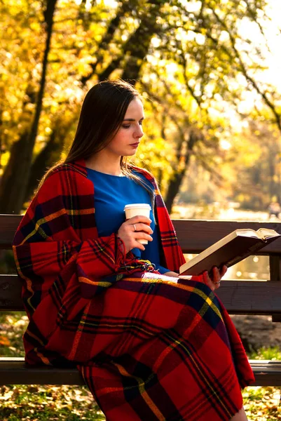 Young girl with book and coffee in autumn park