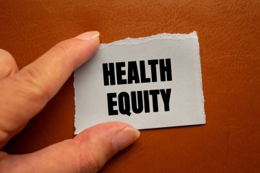 Health Equity message written on ripped torn white paper piece on brown background. Conceptual Health Equity symbol. Copy space.