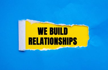 We Build Relationships message written on ripped torn blue paper on yellow background. Conceptual We Build Relationships symbol. Copy space.