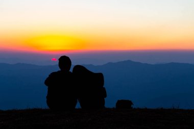 Gün batımı arka plan ile Dağı'nda oturan tatlı çift siluet