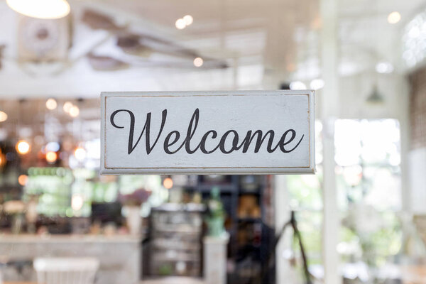 Welcome label is it make of old wood. Добро пожаловать табличка крупным планом через стекло двери кофейни
.