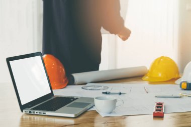 Mimar arka plan ile ofiste ahşap masa üzerinde bir fincan kahve ve plan ile boş boş ekran dizüstü bilgisayar