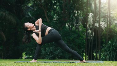 Parsva Bakasana için hazırlık pozisyonunda yoga yapan Asyalı kadın açık hava parkında paspasın üzerinde Crane Poz veriyor..