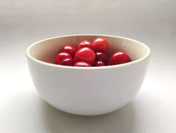 Taze kırmızı kirazlar sade beyaz arka plandaki küçük yuvarlak taş kaplara yerleştirilip yerleştirildi..