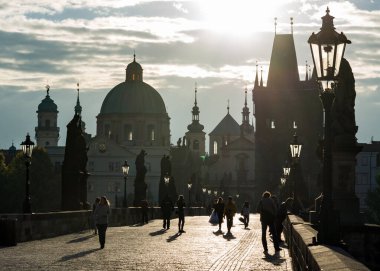 PRAG, CZECH Cumhuriyet - 09 Eylül 2013: Charles Köprüsü 'nü (Karluv Most) sabah erken saatlerde geçen birkaç kişi. Gün doğumunda Eski Şehir Köprüsü Kulesi ve St. Francis Seraph Kilisesi manzarası.