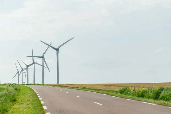 Turbinas eólicas de uma usina para geração de eletricidade perto da estrada rural na Normandia, França. Paisagem rural. Produção de electricidade respeitadora do ambiente — Fotografia de Stock