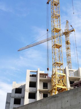 Sarı kule vinç mavi gökyüzü karşı bir gri beton çit arkasındaki bina yeni bir yüksek katlı üzerinde çalışıyoruz