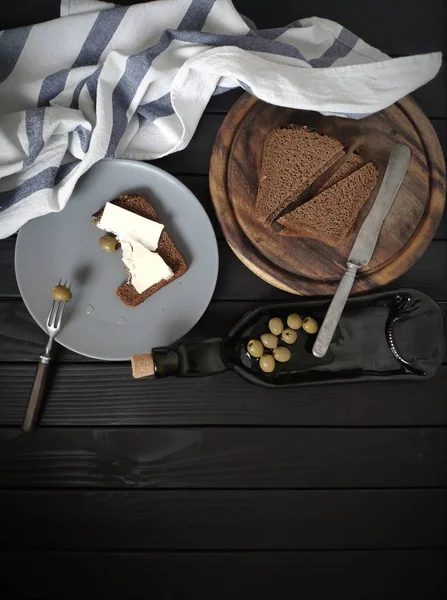 Minimalistic composition on a black wooden background, black bread, oil and olives.