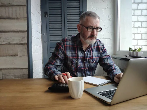 A male accountant works on a laptop and counts on a calculator.