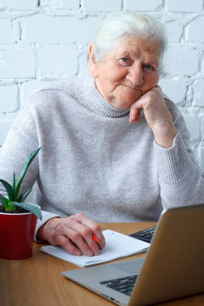 Стара жінка сидить за столом перед ноутбуком . — стокове фото
