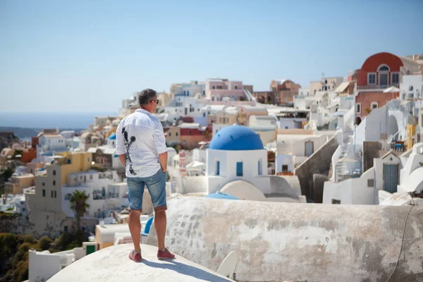 Man stands amid the architecture of Santorini and looks at his watch