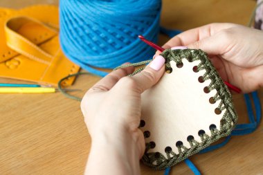 Genç bir kadının elleri, açık ahşap bir yüzeyde yeşil iplikten tığ işi örme. Yeni bir iplik çantası başlatın.