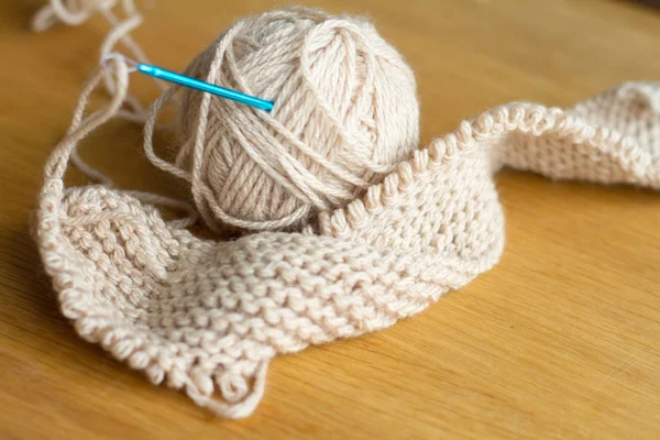 Close-up knitting from beige yarn, needle, crochet hooks. Work on a new product. Selective soft focus. — Stock Photo, Image