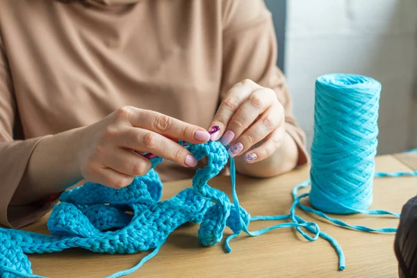 Manos de una mujer joven tejer ganchillo de hilo azul sobre una superficie de madera clara. Iniciar una nueva bolsa de hilo . —  Fotos de Stock