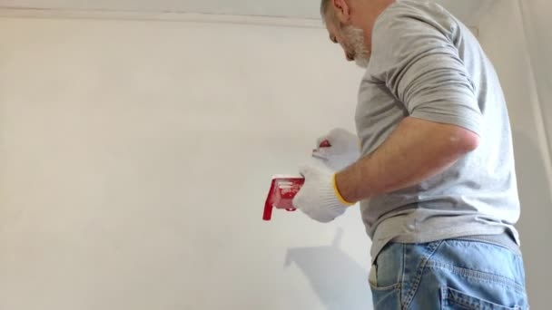 4k baard man schilderij interieur muren op flat met behulp van verfborstel. Knappe jonge man doet reparaties-actief schildert muur met witte verf. — Stockvideo