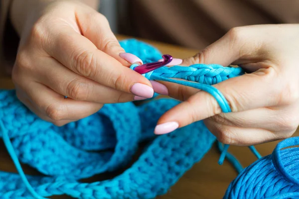 Die Hände einer jungen Frau stricken Häkeln aus blauem Garn auf einer hellen Holzoberfläche. eine neue Tüte Garn starten. — Stockfoto