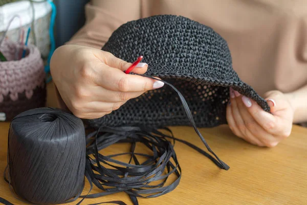 Manos de una joven mujer tejer sombrero de hilo sintético negro en una superficie de madera clara. Enfoque suave selectivo —  Fotos de Stock