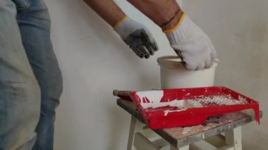 Gri saçlı sakallı bir adam bir kova bir sopa ile beyaz boya karışımları ve konteyner içine, bir odada duvar boyama için hazırlama.