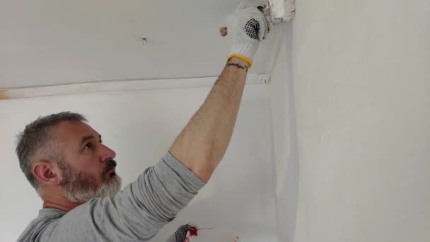 髭の男は ペイントブラシを使用してフラットで内壁を塗装します 修理をしてハンサムな若い男 積極的に白いペンキで壁を塗ります ホームリノベーションまたは模様替えコンセプト — ストック動画