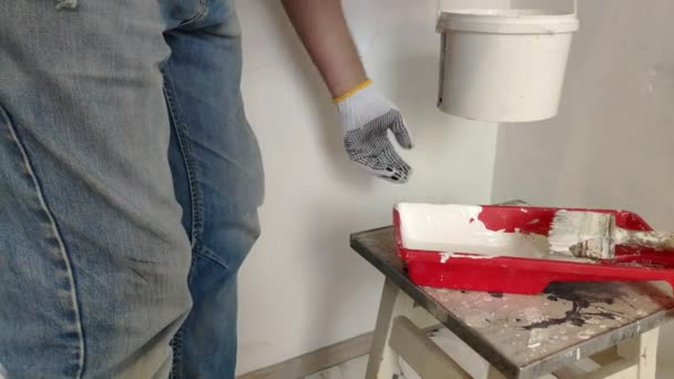 一个头发花白的胡须男人用棍子把水桶里的白色油漆混合在一起 倒进容器里 准备在房间里粉刷墙壁 — 图库视频影像