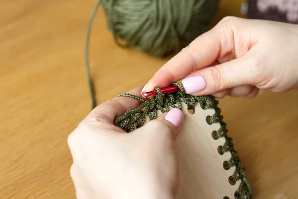 Hands of a young woman knit crochet from green yarn on a light wooden surface. Start a new bag of yarn. — Stock Photo, Image