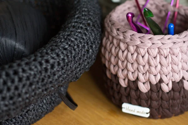 Two-tone knitted basket on a light wooden surface against the background of knitting and details for making handmade knitted bags. — Stock Photo, Image