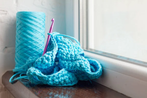 Stricken aus hellblauem Garn und einem Häkelhaken auf einem dunklen Fensterbrett vor einer weißen Ziegelwand. Selektiver weicher Fokus. — Stockfoto