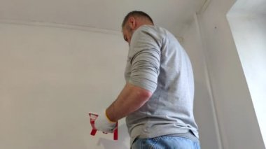 4k sakallı adam boya fırçası kullanarak düz iç duvarlar resim. Yakışıklı genç adam tamir yapıyor-aktif beyaz boya ile duvar boyaları. Ev Renovasyonu veya yeniden dekorasyon konsepti.