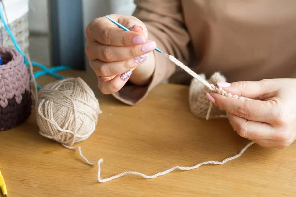 Mãos de uma jovem mulher tricô crochê de fios de bege em uma superfície de madeira leve. Comece um novo saco de fios . — Fotografia de Stock