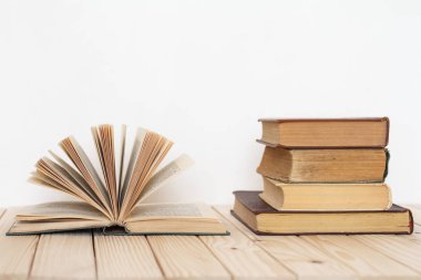 Açık bir kitap, beyaz bir duvara karşı ahşap bir yüzey üzerinde Vintage kitap yığını yanında.