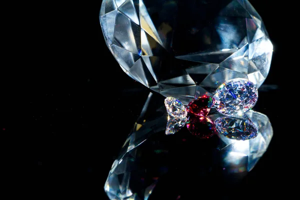 Τεράστιο διαμάντι και αρκετοί σικ κρύσταλλοι σε ένα μαύρο καθρέφτη επιφάνεια, λάμψη και λάμψη. — Φωτογραφία Αρχείου