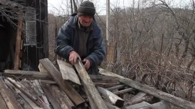 Çok yaşlı bir adam bir kulübeyi onarmak ya da ateşi yakmak için tahtaların üzerinden geçiyor, savaştan sonraki hayat, üçüncü dünya ülkeleri, yoksulluk sınırının altındaki hayat.