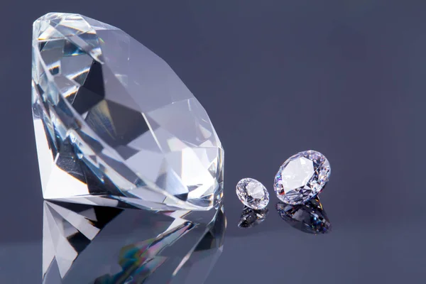 Riesiger Diamant und mehrere schicke Kristalle auf einer grauen Spiegeloberfläche, schimmern und funkeln — Stockfoto