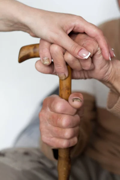 Primo piano di mani di uomini anziani e giovane badante ragazza che si tiene per mano sul bastone da passeggio . — Foto Stock