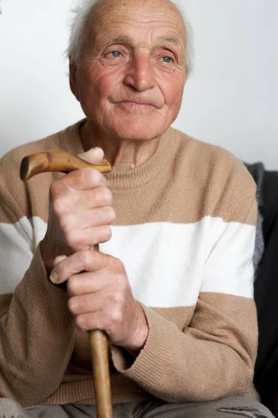 Portret van een lachende oude man die zijn handen op het handvat van een houten stok zetten. — Stockfoto