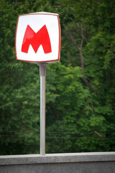 La gran letra roja M indica la entrada al metro subterráneo sobre el fondo de un parque verde —  Fotos de Stock