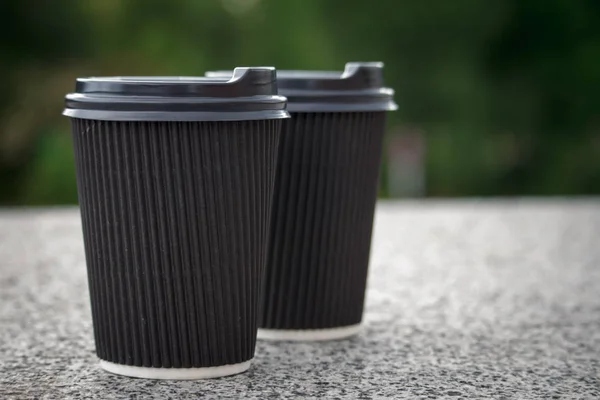 Two black disposable cups of coffee with lids are standing on the stone parapet