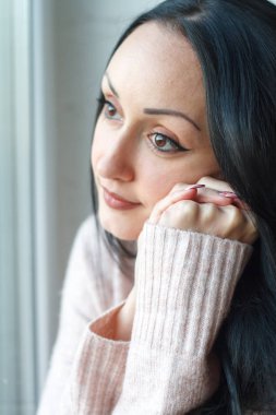 Closeup uzun siyah saçlı gülümseyen güzel genç kadın pencereden dışarı bakar, pencereye yansıyan