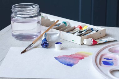 Suluboya seti, fırçalar, bir bardak su ve beyaz bir levha üzerinde bir palet, güzel suluboya darbeleri