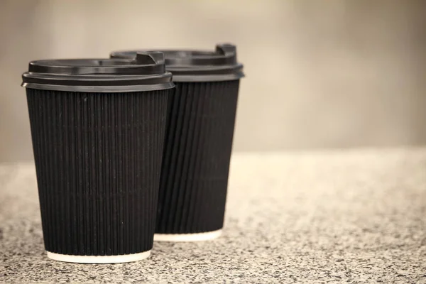 Две черные одноразовые чашки кофе с крышками стоят на каменном парапете — стоковое фото