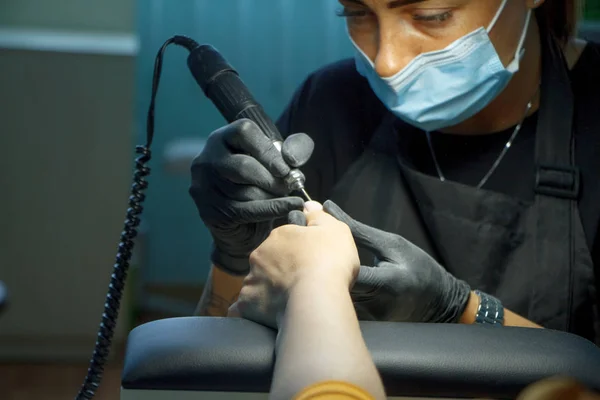 Kosmetikerin mit Maske in schwarzen Handschuhen macht Nägel weibliche Kundin für eine Maniküre mit Gel-Bezug — Stockfoto