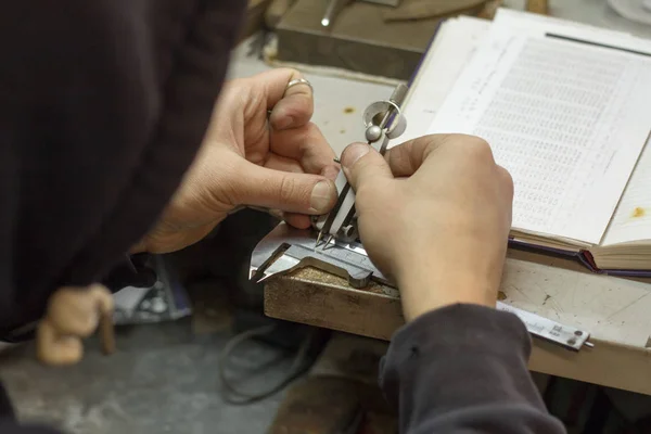 The master jeweler holds the working tool in his hands and makes jewelery at his workplace