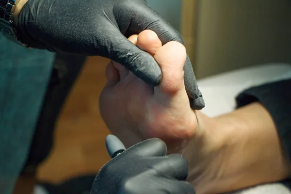 Pediküre Meister während der Arbeit. Nahaufnahme weiblicher Füße und Hände in Handschuhen mit einer speziellen Werkzeugmaschine. — Stockfoto