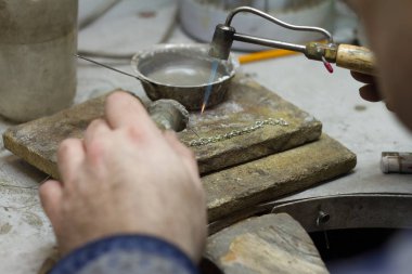 Usta kuyumcu elinde çalışma aracı tutar ve işyerinde mücevher yapar